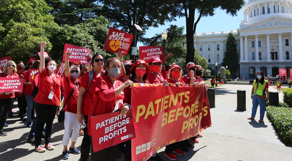Group of nurses marching towards CA Capitol building, holding banner "Patients over Profits"