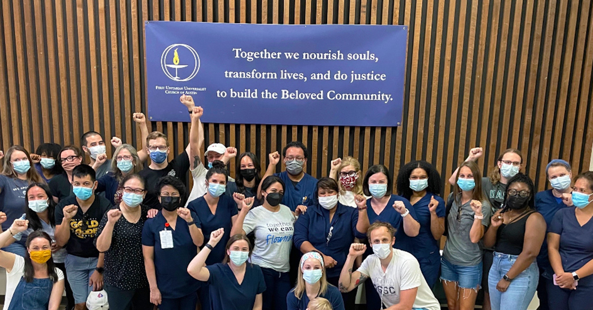 Large group of nurses with raised fists in front of sign "Together we nourish souls, transform lives, and do justice to build the Beloved Community
