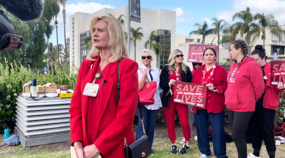 Nurse stands in front of TV camera, others stand behind 