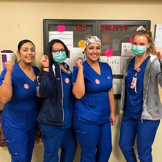 Four nurses inside hospital smiling and holding raised fists