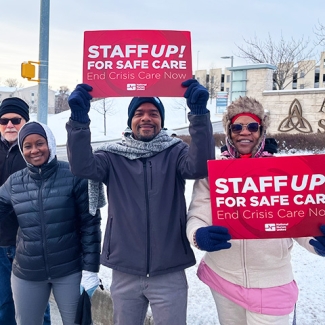 Group of 3 nurses outside in cold weath holding signs "Staff Up For Safe Patient Care"