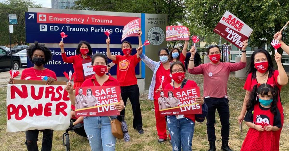 Nurses and community members in front of Cook County Health hospital holding signs "Safe Staffing Save Lives" and "Nurse Power"