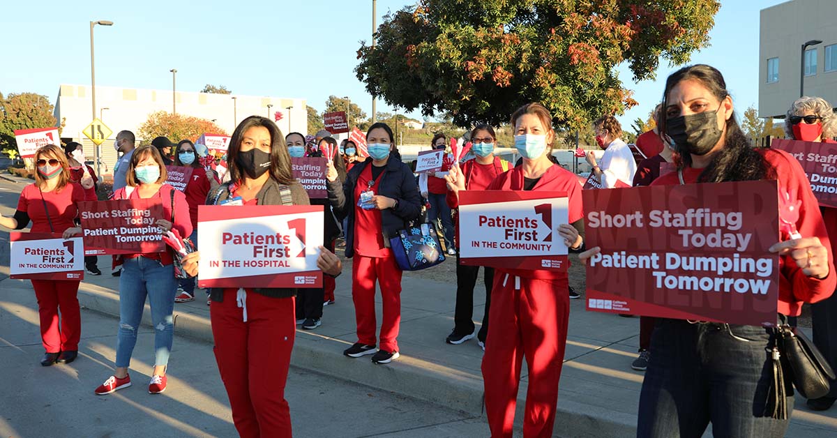 Large group on masked nurses outside holding signs calling for patient safety.