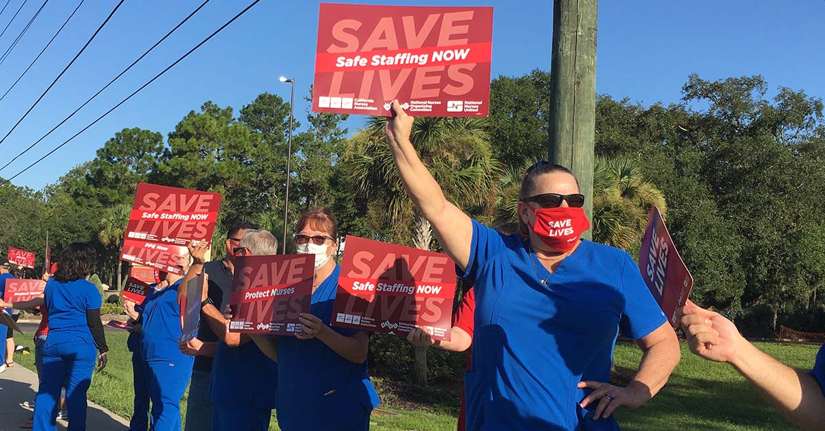 Nurses outside along road hold signs "Save Lives: Safe Staffing Now"