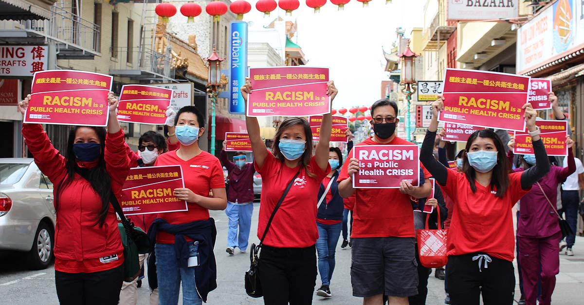 Group of nursews march through streets holding signs "Racism is a Public Health Crisis"