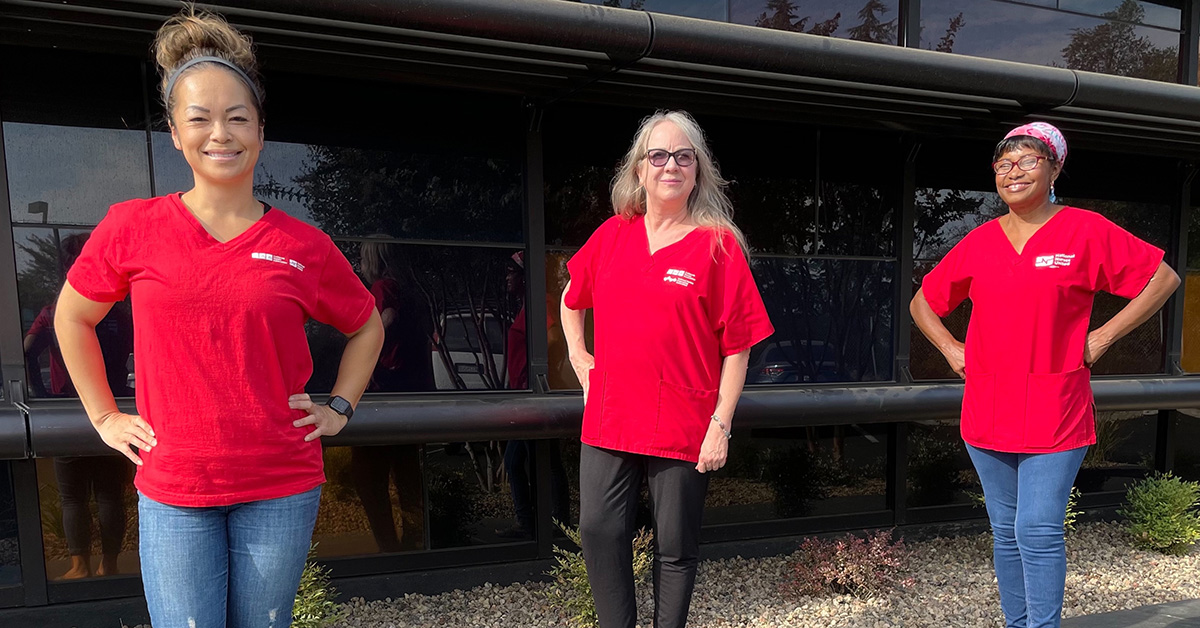 Group of three nurses outside wearing red scrub shirt.