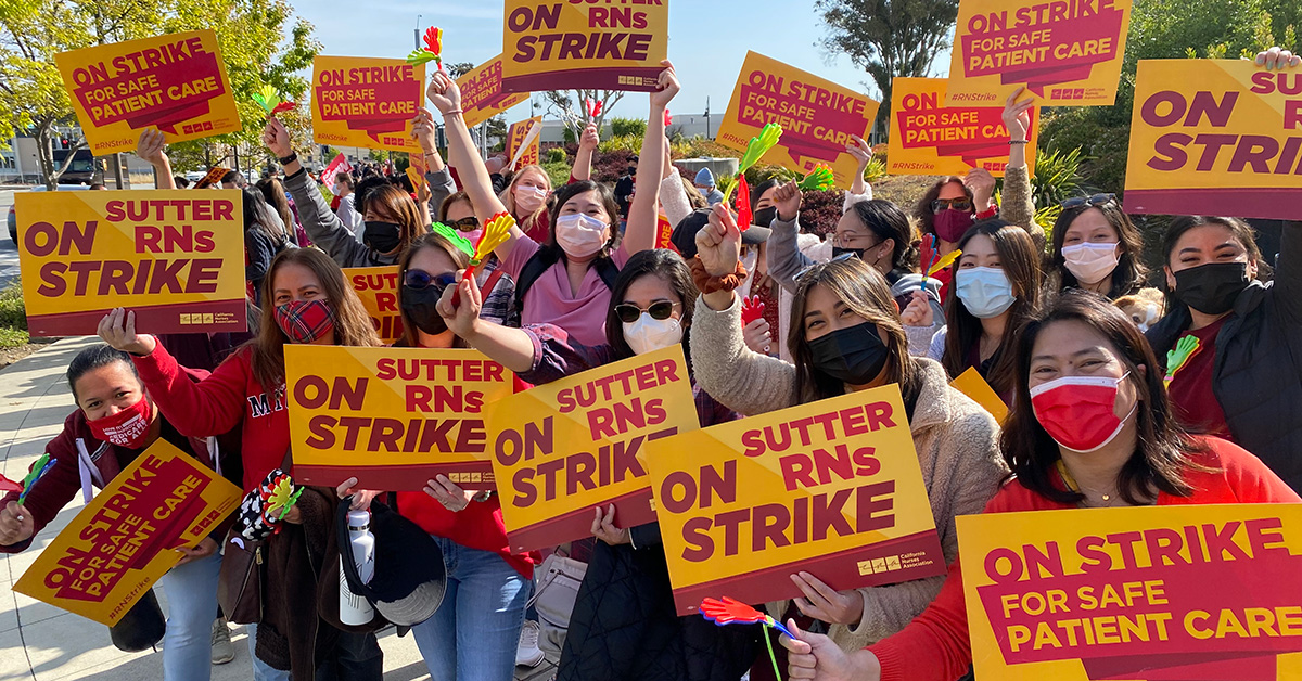 Large group of nurses outside hold signs "Sutter RNs On Strike"