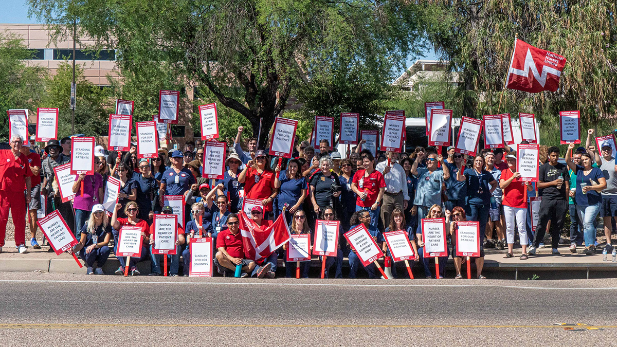 Large group of nurses outside hold signs "Standing for our patients"