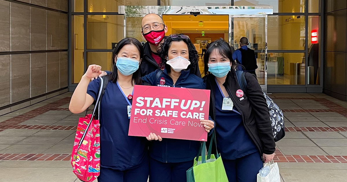 Group of four nurses outside hospital hold sign "Staff up for Safe Care"