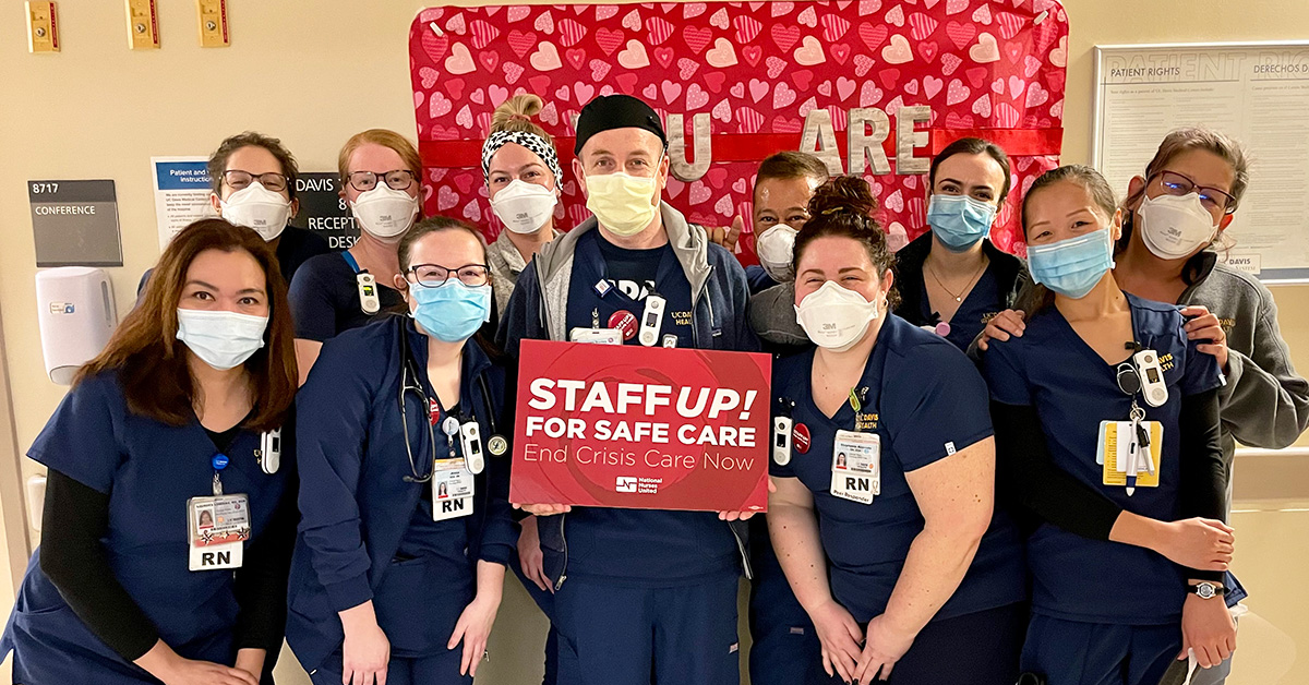 Large group of nurses inside hospital, one holds sign "Staff Up for Safe Care"