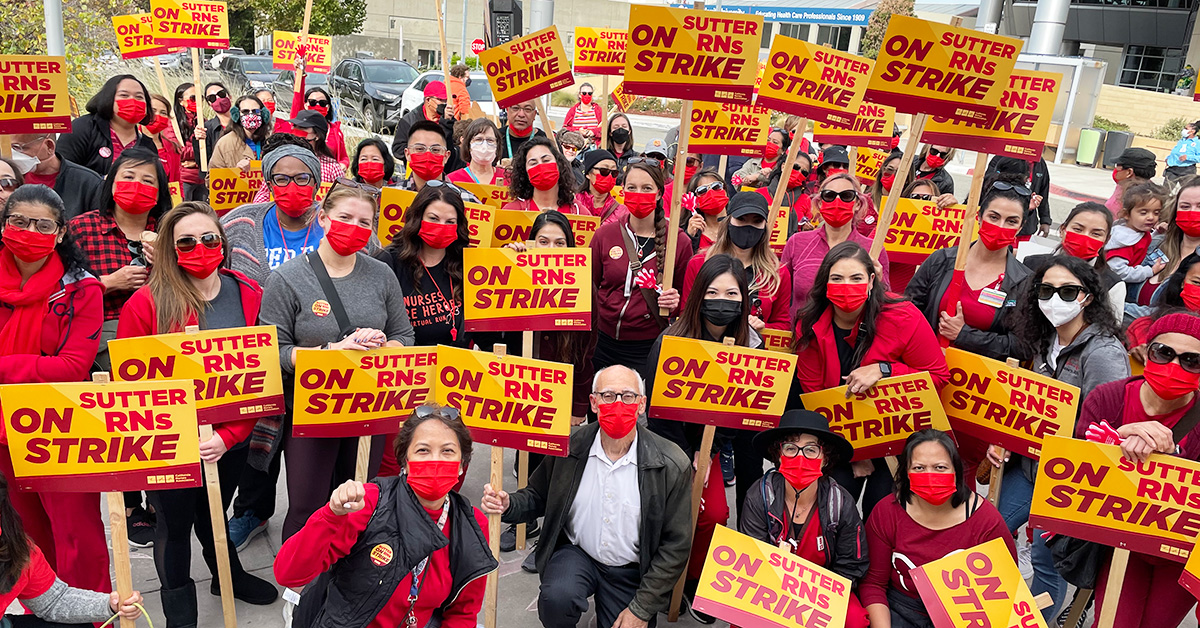 Large group of nurses outside hold signs "Sutter RNs On Strike"