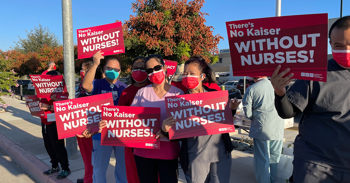Group of nurses hold signs "There's no Kaiser without nurses"