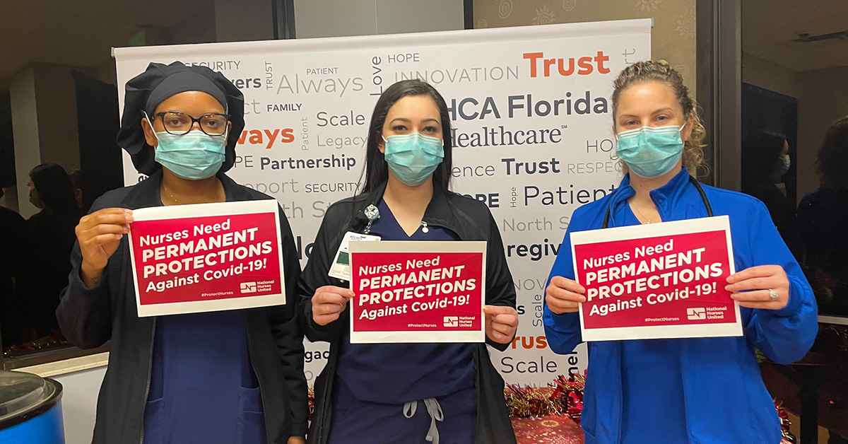 Three nurses hold signs calling on OSHA to enact permanent protections against Covid-19