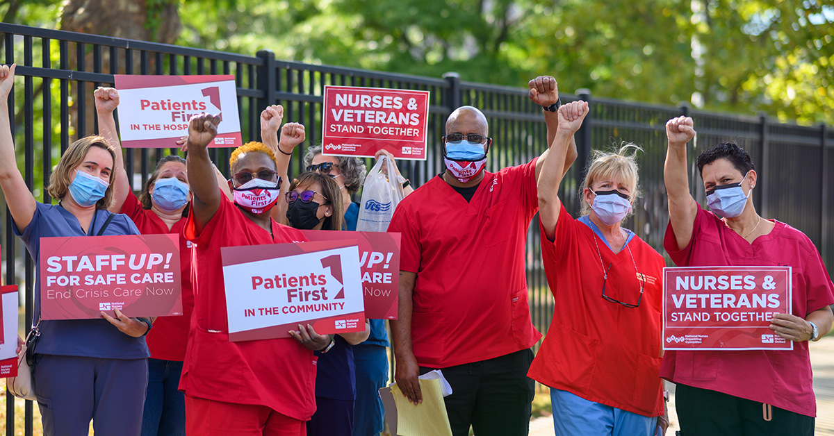 Group of nurses outside hold signs "Nurses and veterans stand together"