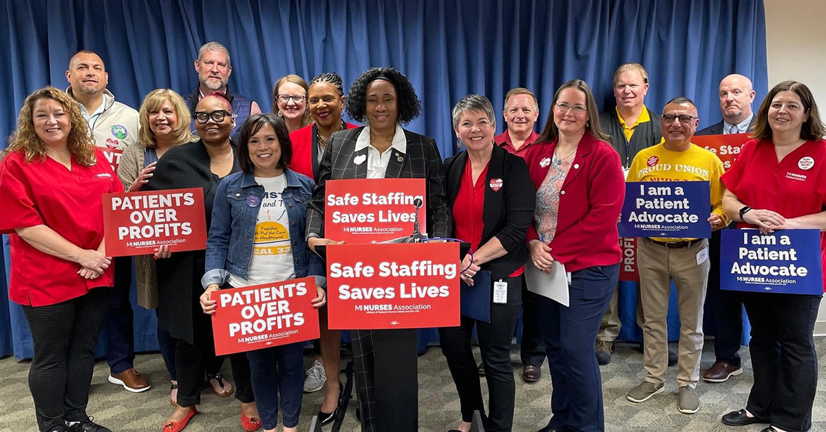 Group of nurses stand at podium holding signs "Safe Staffing Saves Lives"
