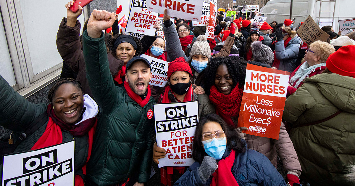 Large group of nurses cheering on picket line, some with raised fists