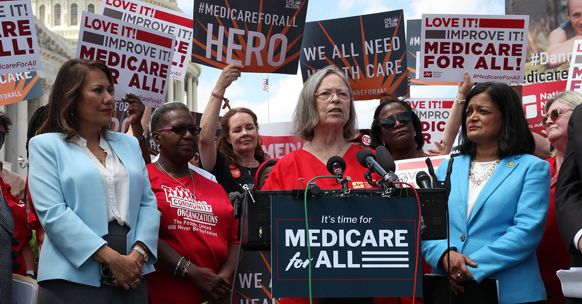 NNU President Deborah Burger stands at podium surrounded by supporters in front of U.S. Capitol building with "It's time for Medicare for All" sign on podium.