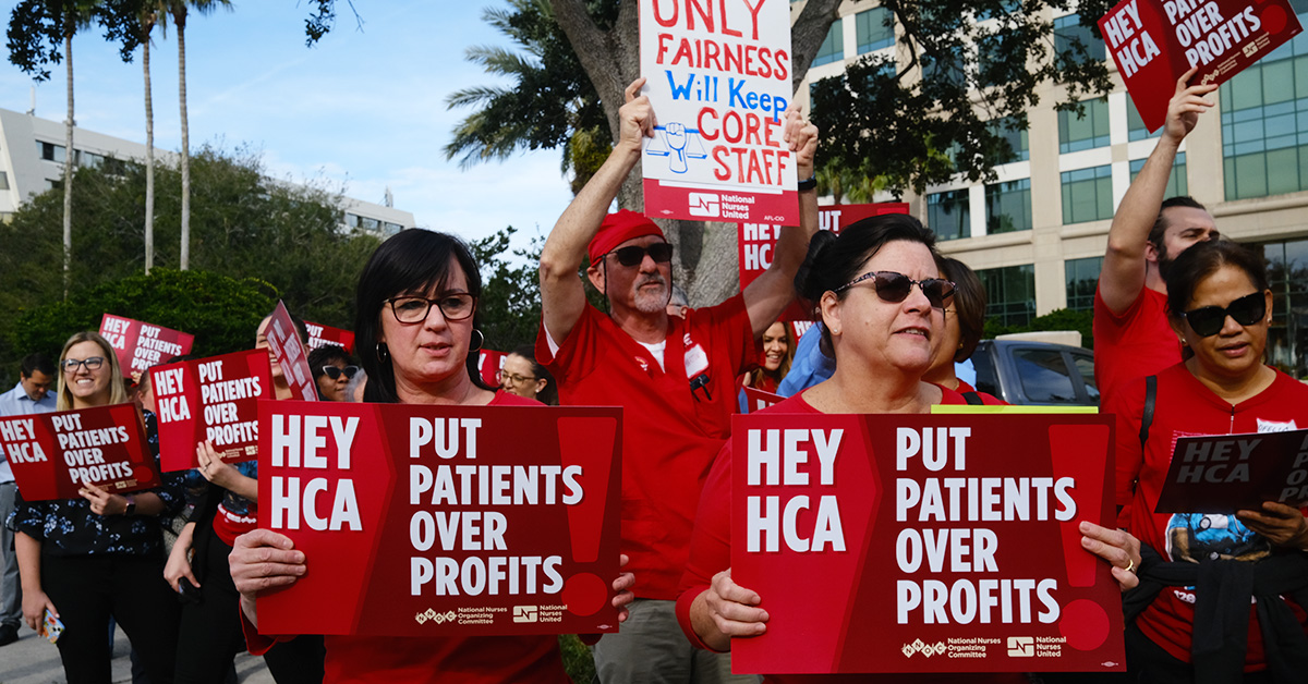 Nurses outside hospital picketing, holding signs "Hey HCA, Put Patients Over Profits"