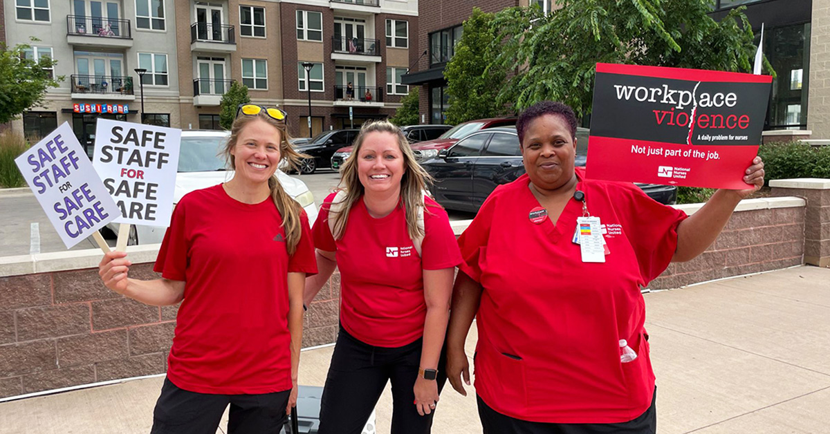 Three nurses outside smiling holding signs calling for safe staffing and workplace violence prevention