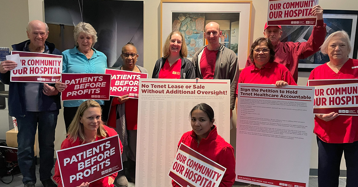 Group of nurses inside hospital hold signs "Patients Before Profits" and "Our Community, Our Hospital"