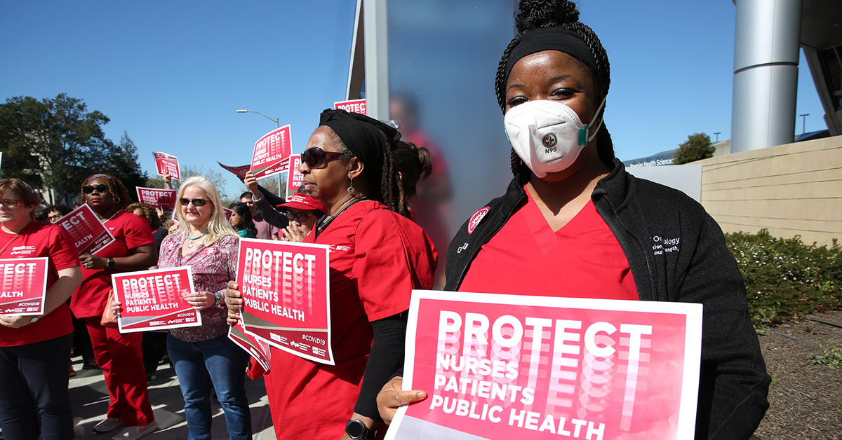 Nurses outside holding signs "Protect Nurses, Patients, Public Health"