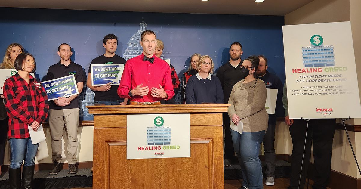 Chris Rubesch, RN standing at podium that has sign "Healing Greed".