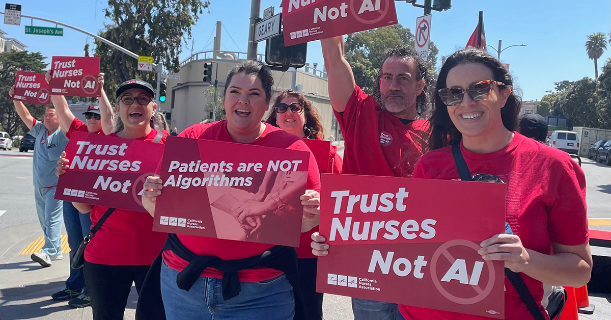 Group of nurses outside holding signs "Patients are Not Algorithms" and "Trust Nurses, Not A.I."
