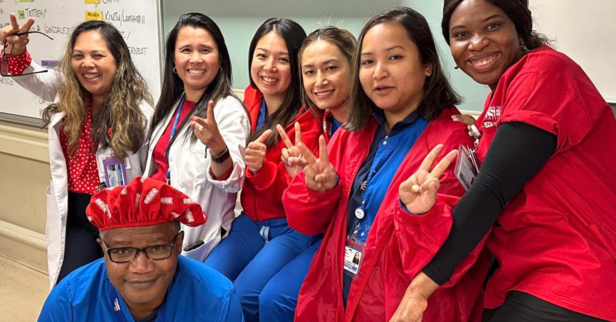 Group of 7 nurses inside hospital posing side-by-side and smiling