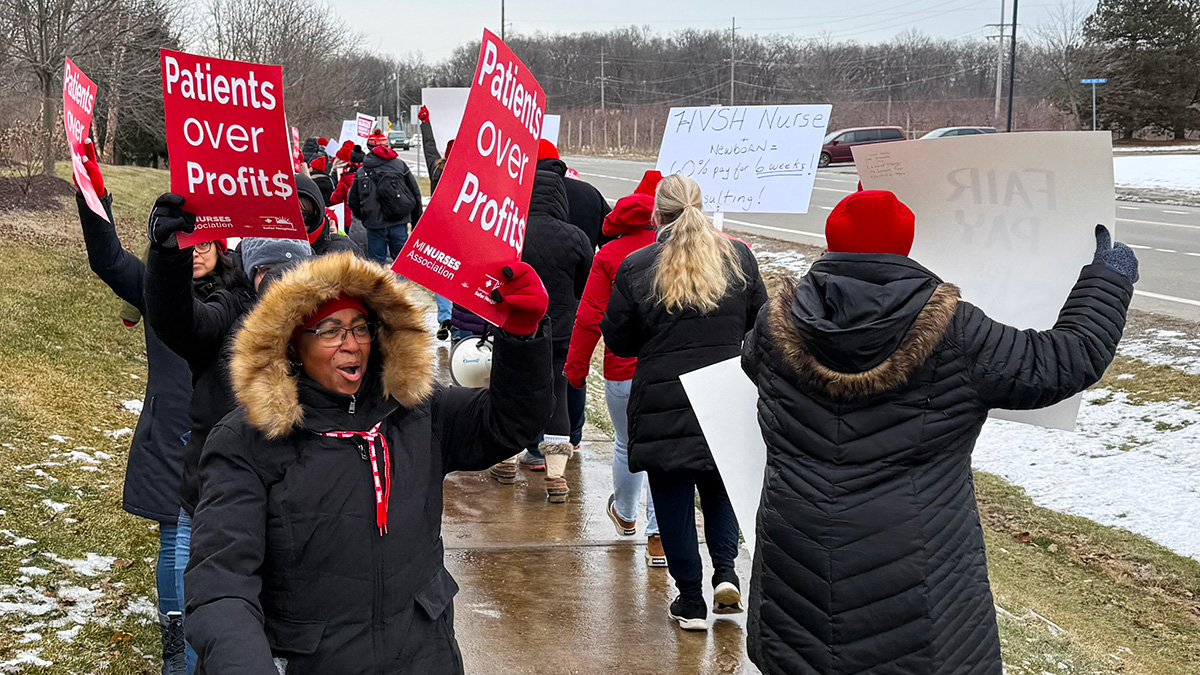 Nurses on picket line in cold weather coats, holding signs "Patients Over Profits"