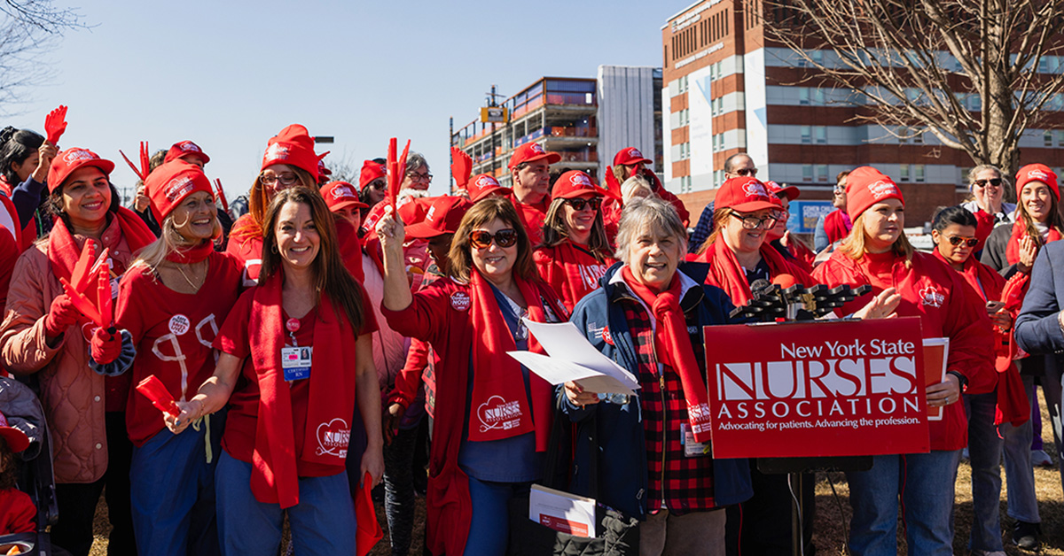 Group of nurses standing together, smiling, holding sign "New York State Nurses Association"