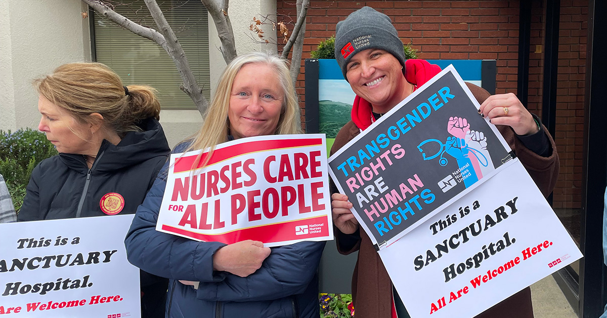 3 nurses outside hospital hold signs "Nurses Care for All People" and "Transgender Rights Are Human Rights"