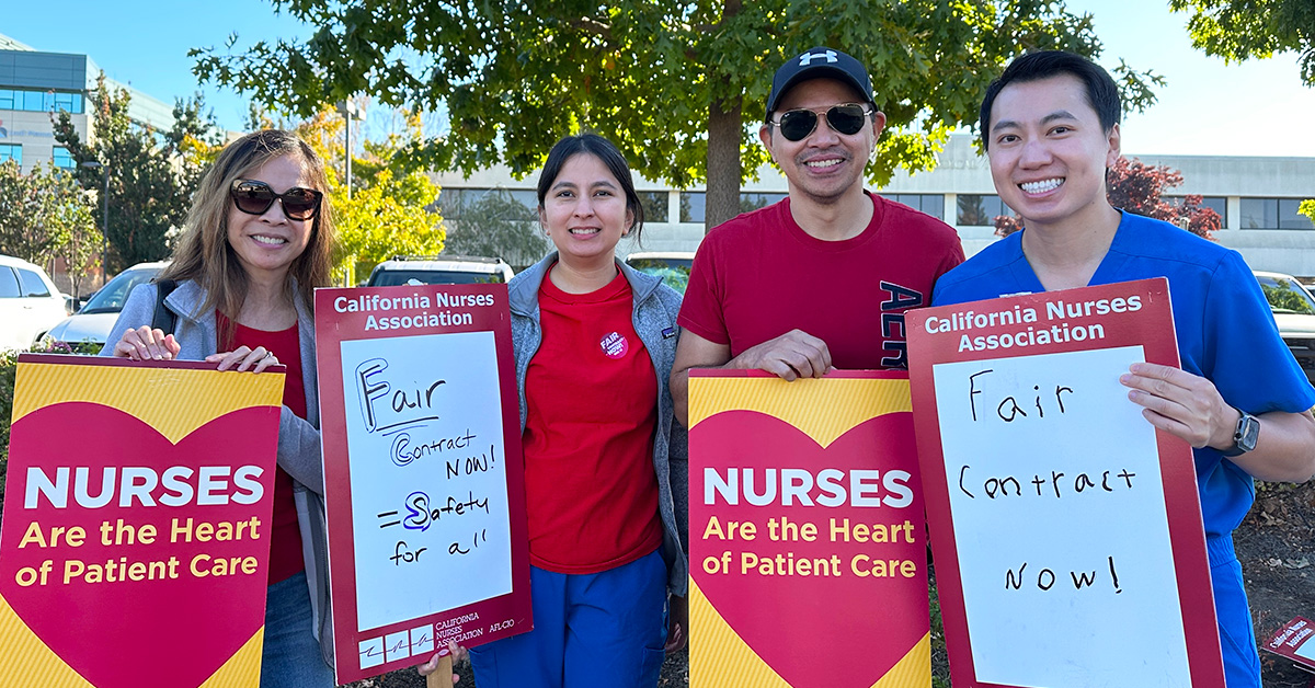 Four nurses outside holding signs "Nurses are the heart of patient care" and "Fair contract now"