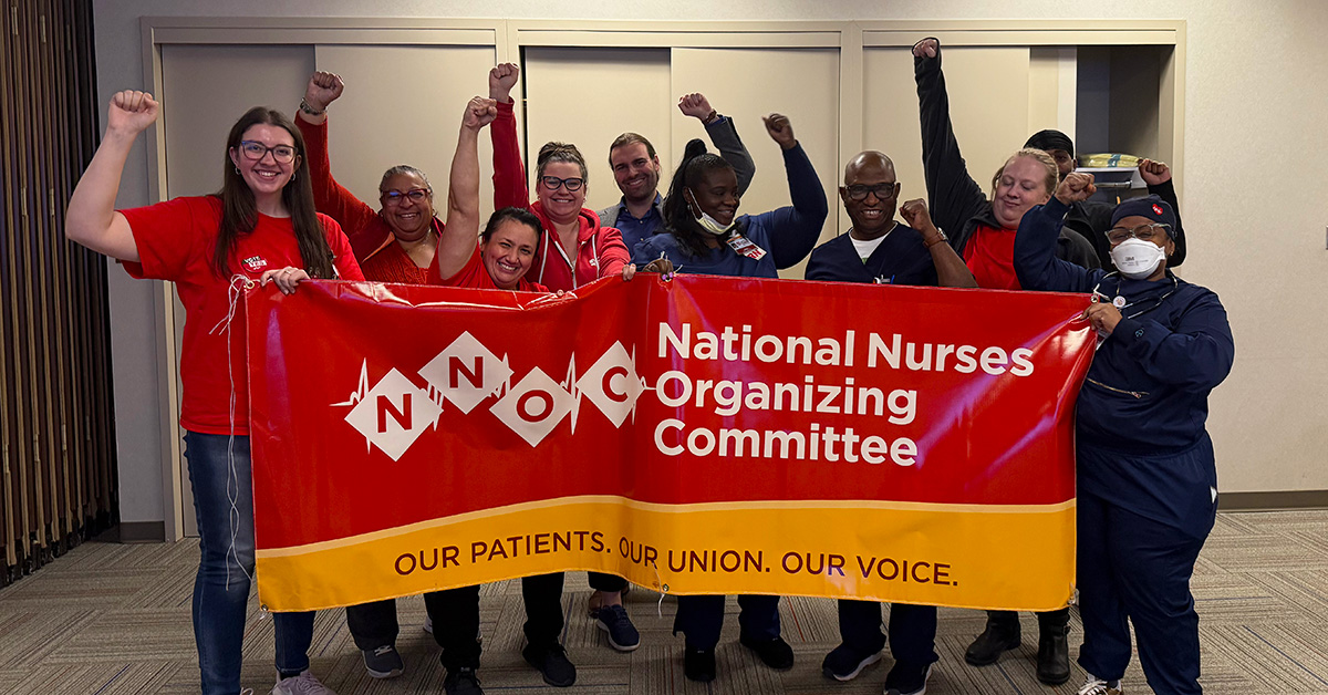 Group of nurses smiling with raised fists, holding banner "National Nurses Organizing Committee"