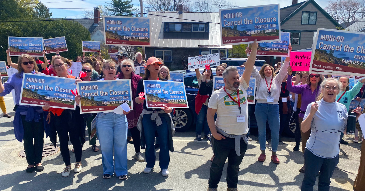 Large group of people outside holding signs "Cancel the Closure"