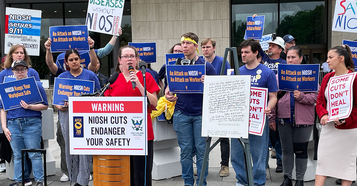 Nurse at podium, behind them health care workers holding signs "An Attack on NIOSH = Attack on workers"