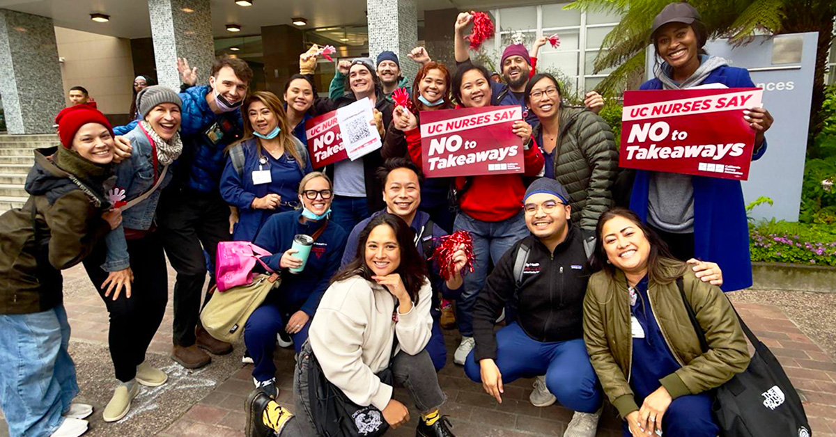 Group of nurses outside, smiling, holding signs "UC Nurses Say No To Takeaways"