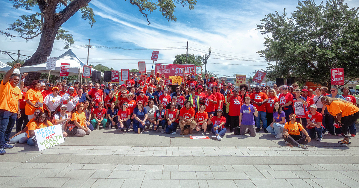 Large group of nurses outside behind banner "NOLA Nurses On Strike"