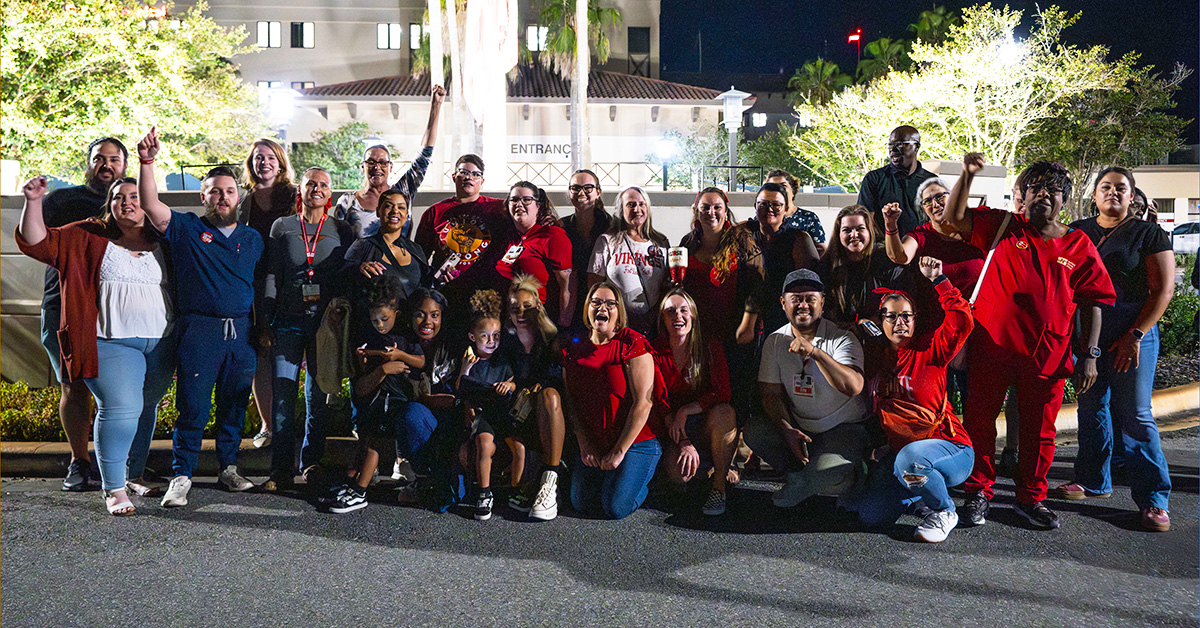 Large group of nurses outside hospital, smiling, with raised fists