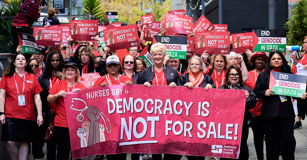 Large group of nurses marching, holding banner "Democracy is NOT for Sale"