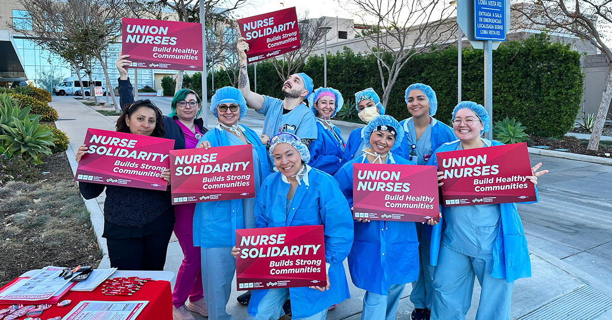 Group of nurses outside hospital, holding signs "Union Nurses" and "Nurse Solidarity"