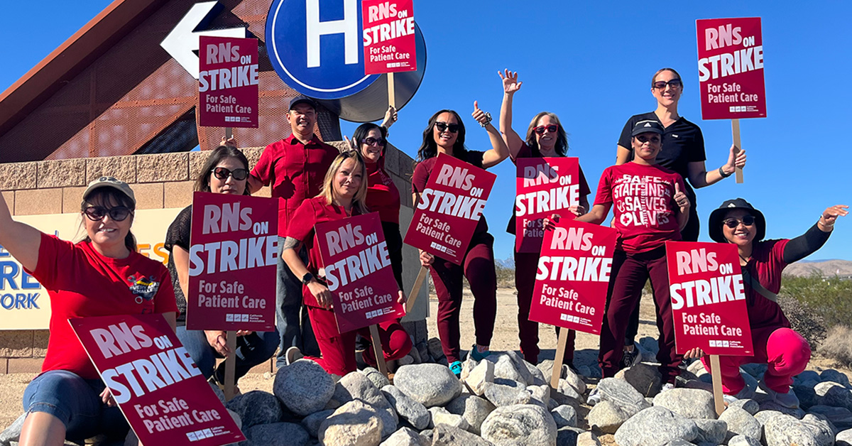 Group of nurses outside, on rocks, holding signs "RNs on strike for safe patient care"