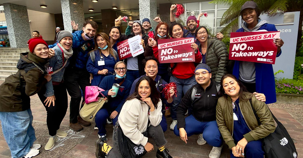 Group of nurses outside hospital smiling, holding signs "UC nurses say no to takeaways"