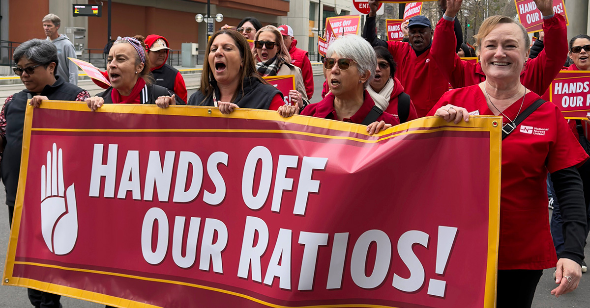 Nurses marching in street holding banner "Hands Off Our Ratios"