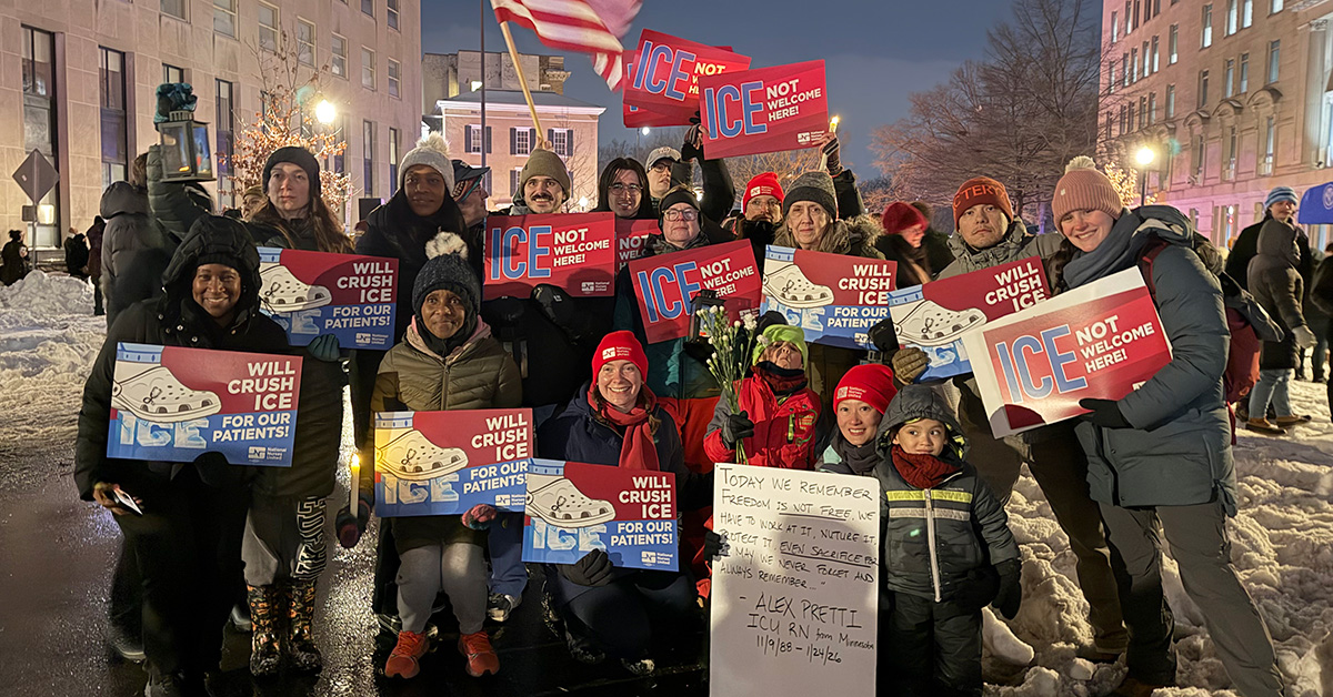 Large group of nurses outside, wearing cold weather clothing, smiling, holding signs "ICE Not Welcome Here" and "Will Crush ICE for Our Patients"