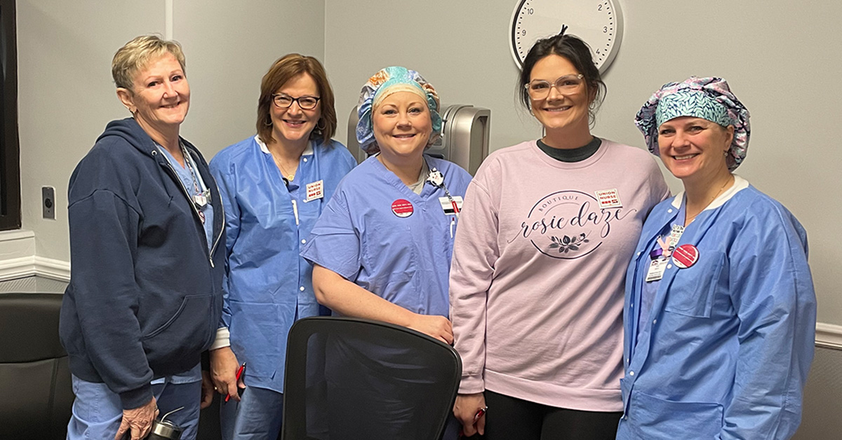 Four nurses inside hospital, standing side-by-side, smiling
