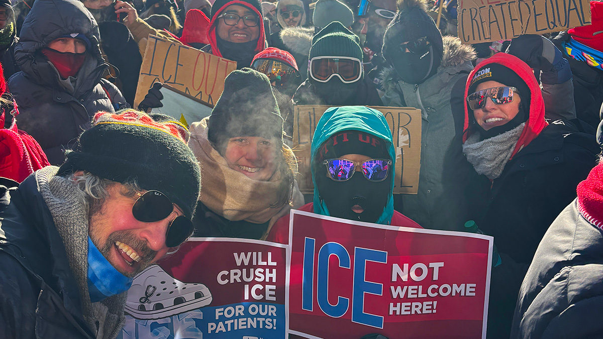 Group of nurses outside, wearing winter clothing, holding anti-ICE signs