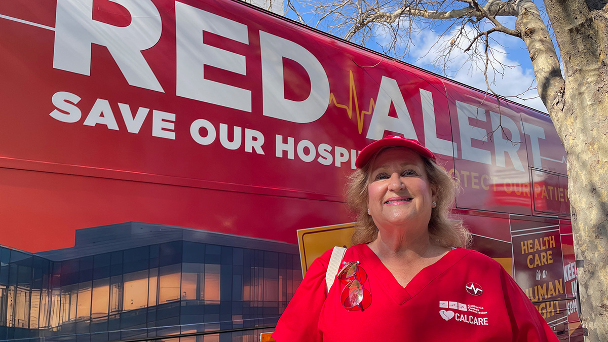 CNA President Sandy Reding, in red scrubs, smiling, in front of Red Alert tour bus