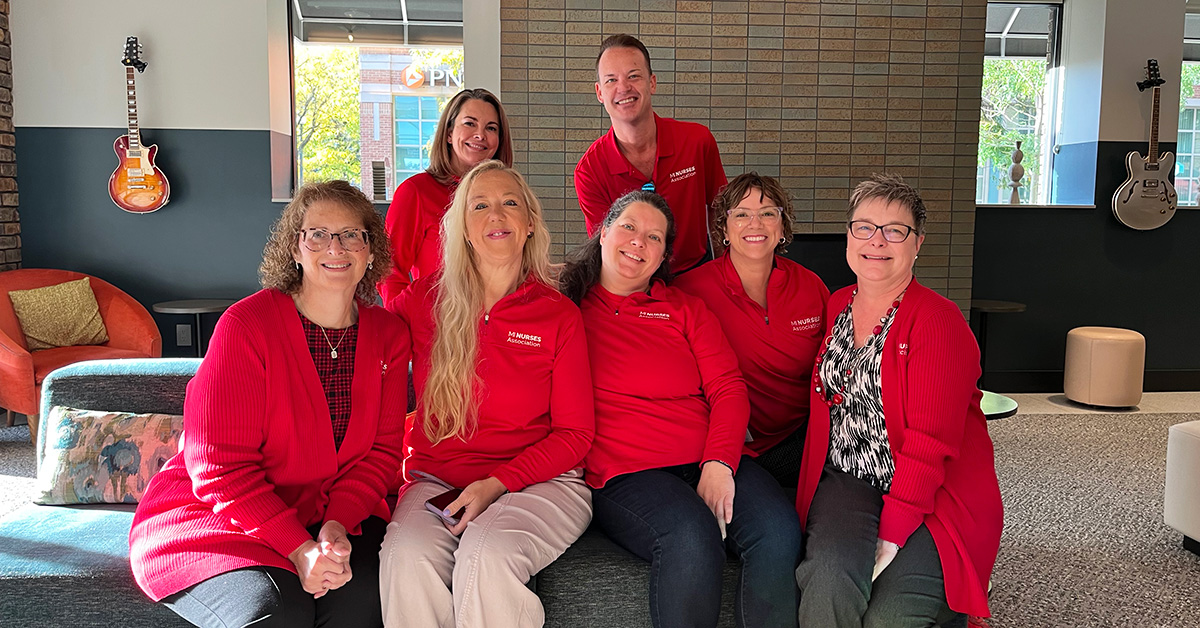Group of seven nurses sitting and standing together, smiling, wearing red, inside