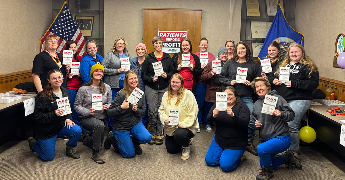 Large group of nurses inside posing together, smiling, holding contracts
