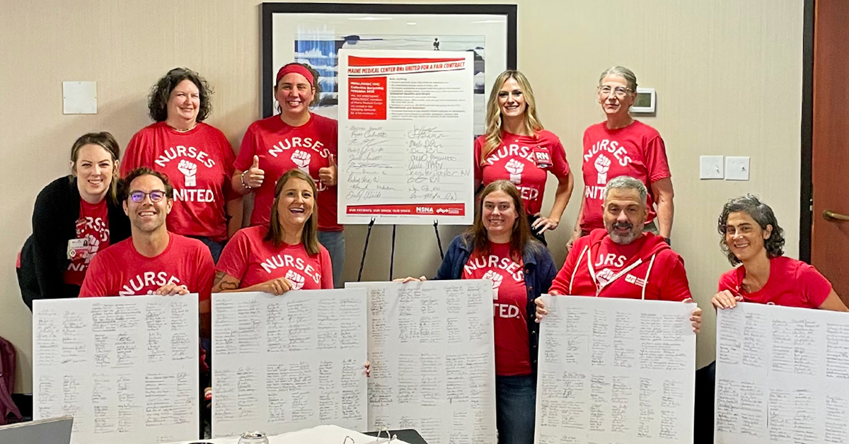 Group of nurses inside, smiling, holding large print outs of petition signer lists